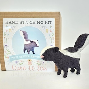 May include: A hand stitching kit to make a felt skunk. The kit includes all the materials needed to create a small, black and white skunk with a pink nose. The box has a colourful design with the text "HAND STITCHING KIT" and "FELT SKUNK SEWING".