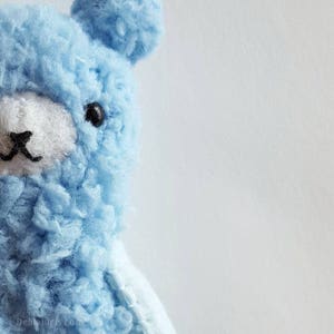 May include: A light blue plush toy shaped like a bear with black eyes and a white nose. The bear is facing the left side of the image.