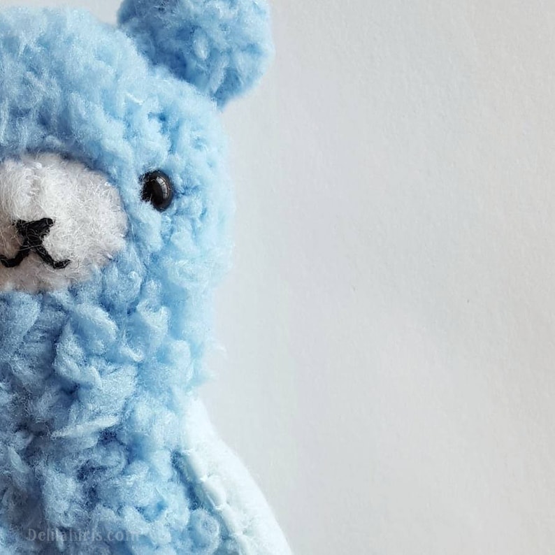 May include: A light blue plush toy shaped like a bear with black eyes and a white nose. The bear is facing the left side of the image.