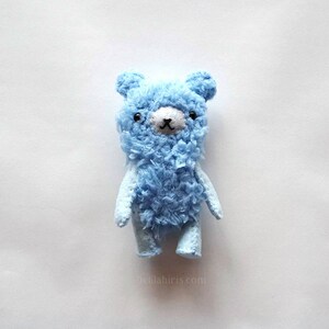 May include: A small, blue, fuzzy teddy bear with black eyes and a black nose.