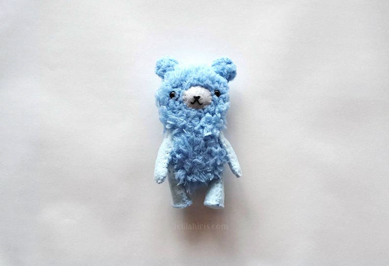 May include: A small, blue, fuzzy teddy bear with black eyes and a black nose.