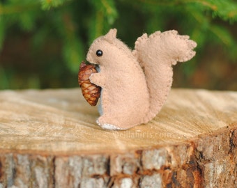 May include: A small, brown felt squirrel holding a brown pine cone. The squirrel is sitting on a wooden stump.