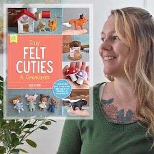 May include: A book cover with the title "Tiny Felt Cuties & Creatures" by Delilah Iris. The cover features a variety of small felt animals and objects, including a fox, a cat, a mushroom, a house, and a coffee cup.