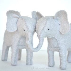 May include: Two gray felt elephant toys with stitched details, standing side by side with their trunks touching.
