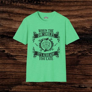 May include: Green t-shirt with a black graphic design that says "When the DM smiles it's already too late". The graphic features a 20-sided die and a dragon.