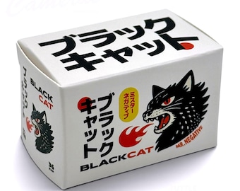 Puede incluir: Una caja de cartón rectangular blanca para película Black Cat con texto en japonés, un gráfico de una cabeza de gato negro con ojos rojos escupiendo fuego y el texto Mr. Negative. La caja incluye el número 36 y el texto Black Cat.