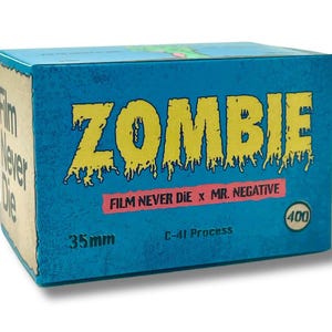 May include: A blue box of 35mm film labeled "ZOMBIE" in yellow, dripping font. The box also features the text "FILM NEVER DIE x MR. NEGATIVE" and "400". The film is C-41 process.