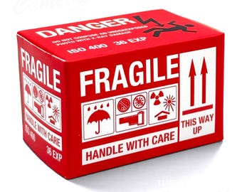 Puede incluir: Una caja rectangular roja para película fotográfica con texto blanco que dice DANGER, FRAGILE, HANDLE WITH CARE, ISO 400 y 36 EXP. La caja presenta iconos gráficos en blanco y negro, incluyendo un paraguas, un carrete y flechas.