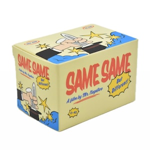 May include: A rectangular box with a cream-colored background and blue trim. The box features the words "SAME SAME" in large red letters, with the phrase "But Different!" in a yellow speech bubble. The top of the box has an illustration of a magician.