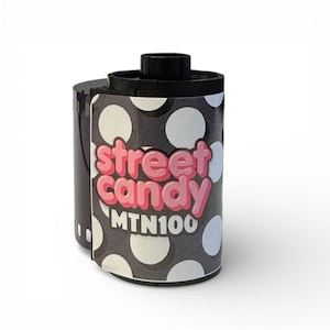 May include: A roll of 35mm film with a black and white polka dot design. The film canister has the words "street candy" in pink bubble letters and "MTN100" in white. The top of the film is black.