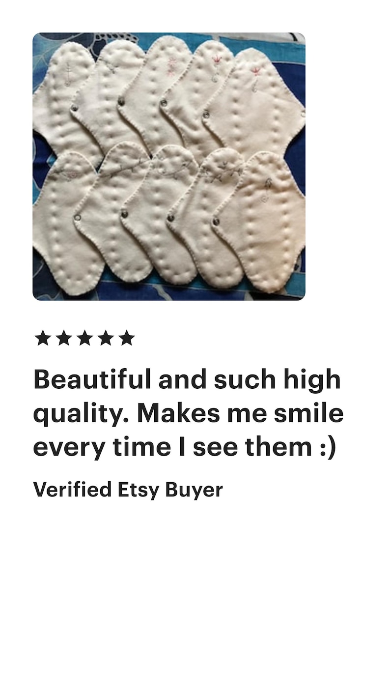 May include: A collection of white, petal-shaped cloth pads with stitched details, arranged on a patterned blue background. The pads are likely reusable menstrual products, designed for comfort and eco-friendliness.
