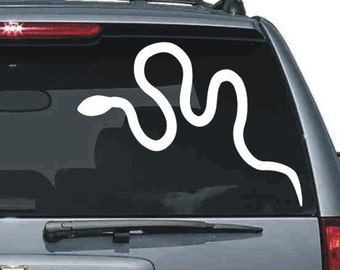May include: White snake decal on a car window. The decal is a stylized outline of a snake, with a curved body and a small head. The decal is applied to the rear window of a vehicle.