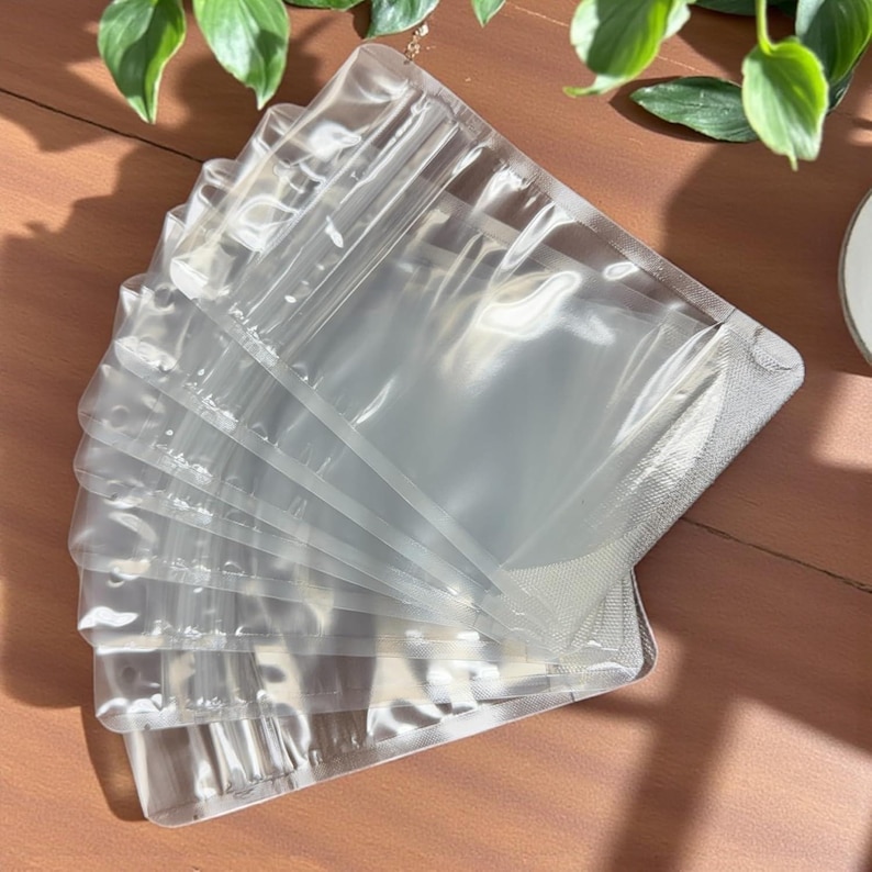 May include: A stack of clear, rectangular plastic pouches arranged in a fan shape. Each pouch features a resealable zipper closure at the top and a heat-sealed bottom edge, providing a transparent view of the contents within the flexible material.
