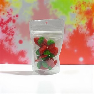 May include: A clear, resealable plastic pouch filled with red and green strawberry-shaped gummy candies. The bag features a zip-lock closure at the top and a small circular hole for hanging, providing a clear view of the colorful fruit-shaped treats.