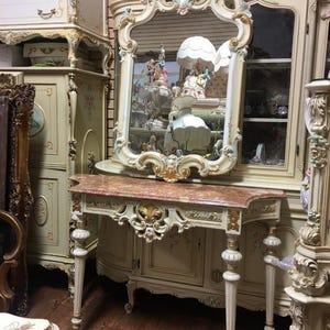 May include: An ornate antique vanity set with a large mirror, a marble top, and decorative carvings. The set is painted in cream with gold accents and floral details, showcasing a classic, elegant design.