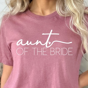 May include: A mauve t-shirt with the text "aunt of the bride" in white lettering.