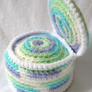 May include: A crocheted box with a lid, featuring a swirling pattern of white, light blue, green, and purple yarn.