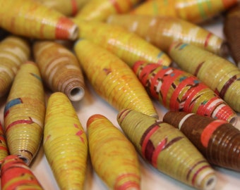 May include: A collection of colorful paper beads, some with patterns, in shades of brown, yellow, and red. The beads are made of rolled paper and are strung together to create a necklace or bracelet.