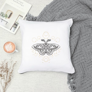 May include: White cushion with a black and white moth illustration surrounded by a geometric pattern of gold circles.