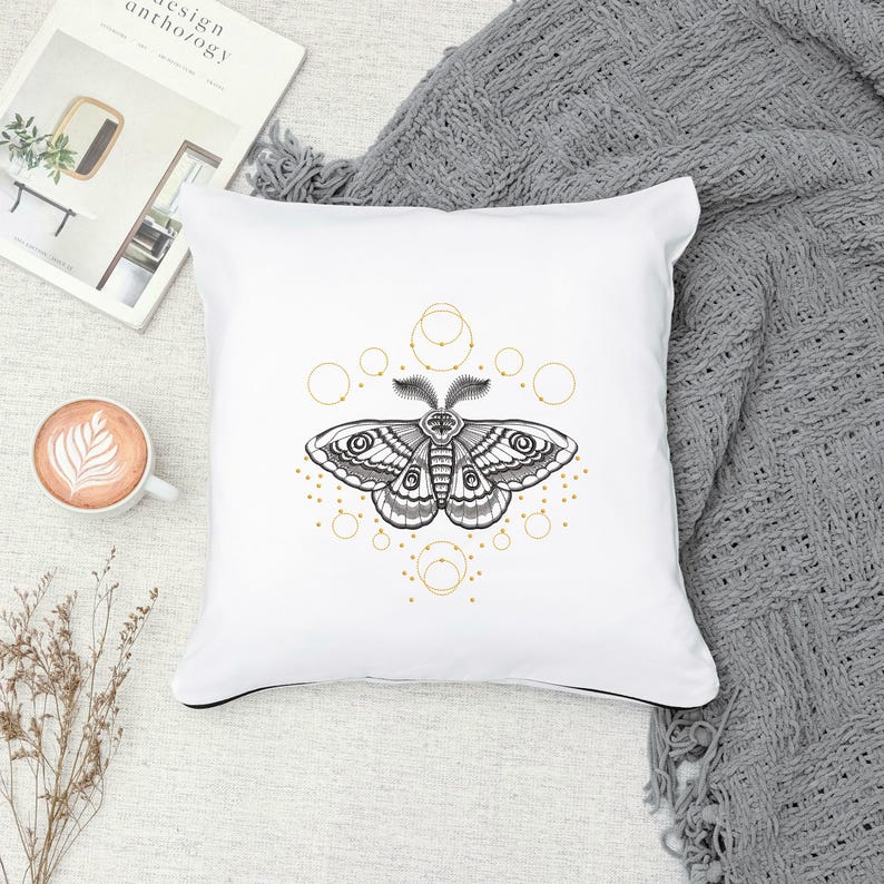 May include: White cushion with a black and white moth illustration surrounded by a geometric pattern of gold circles.