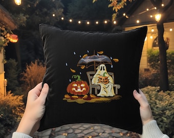 May include: Black square pillow with an embroidered Halloween scene. A ghost and a jack-o'-lantern sit on a bench under an umbrella, with a second jack-o'-lantern nearby. Autumn leaves and raindrops complete the design.