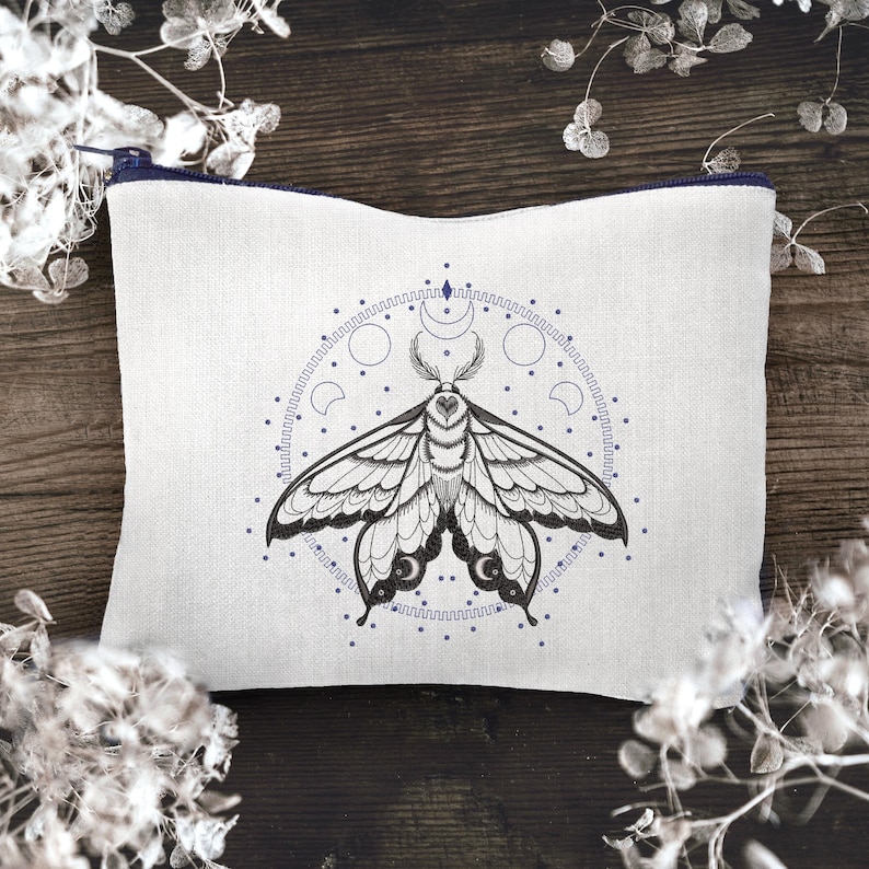 May include: A white linen zippered pouch with a black and white embroidered moth design. The moth is surrounded by a circle of moons and stars.