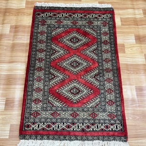 May include: A red and black patterned rug with a geometric design. The rug has a fringe border.