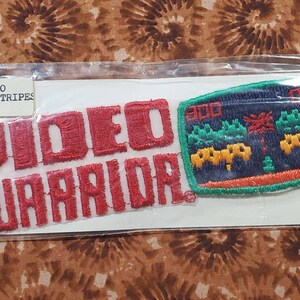 May include: Red embroidered patch with the text "VIDEO WARRIORS" and a smaller patch depicting a video game screen with the text "300" and a pixelated landscape. The text "VIDEO SPORTSTRIPES" is printed on a white label.