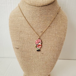 May include: A gold chain necklace with a red and white enamel charm of a girl holding a pink and white polka dot balloon.