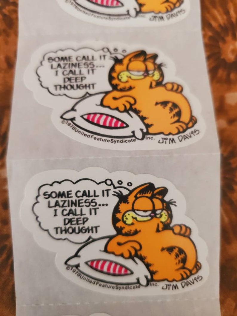 May include: A Garfield sticker featuring a cartoon cat lying on a pillow with the text "Some call it laziness... I call it deep thought." The sticker is white with black outlines and features the copyright information "&copy;1978 United Feature Syndicate Inc. Jim Davis".