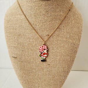 May include: A gold chain necklace with a red and white enamel charm of a girl with a red and white polka dot umbrella.