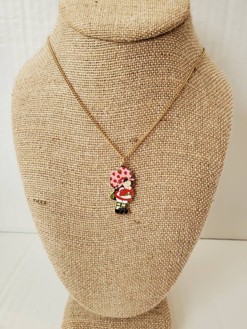 May include: A gold chain necklace with a red and white enamel charm of a girl with a red and white polka dot umbrella.