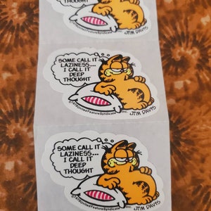May include: Three Garfield stickers with the text "Some call it laziness... I call it deep thought." Garfield is depicted lying on a pillow with his eyes closed. The stickers are white with black outlines and feature the Garfield copyright information and Jim Davis's signature.