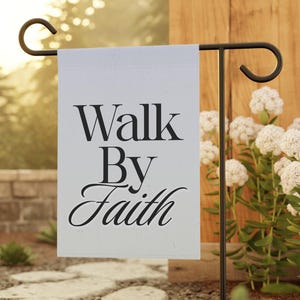 Peut inclure: Un drapeau de jardin blanc avec l'inscription "Walk By Faith" en noir. Le drapeau est suspendu à un piquet de jardin en métal noir. L'arrière-plan comprend un chemin de pierre, de la verdure et une clôture en bois.