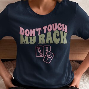 Może przedstawiać: Koszulka w kolorze granatowym z napisem "Don't touch my rack" w kolorze r&oacute;żowym i zielonym. Na koszulce znajduje się r&oacute;żowa ilustracja domina i kostki mahjonga.