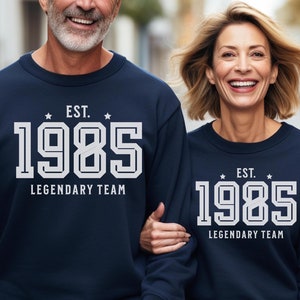 May include: Two people wearing matching navy blue sweatshirts with white text that reads "EST. 1985 LEGENDARY TEAM".