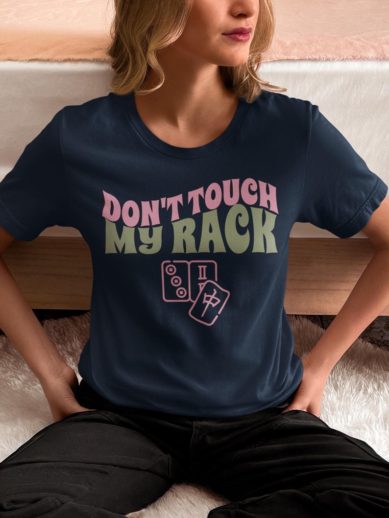 Może przedstawiać: Koszulka w kolorze granatowym z napisem "Don't touch my rack" w kolorze r&oacute;żowym i zielonym. Na koszulce znajduje się r&oacute;żowa ilustracja domina i kostki mahjonga.