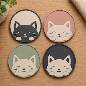 May include: A set of four circular coasters featuring cat illustrations. The top left coaster is beige with a black cat, the top right is pink with a cream cat, the bottom left is sage green with a cream cat, and the bottom right is dark grey with a cream cat.