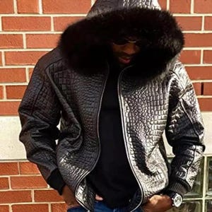 Könnte beinhalten: Eine schwarze Lederjacke mit einer Kapuze, die mit Kunstfell gefüttert ist. Die Jacke hat ein Kroko-Prägemuster.
