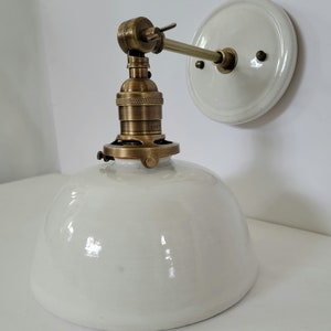 May include: White porcelain wall sconce with a brass socket and arm. The sconce has a white porcelain shade and a round back plate.