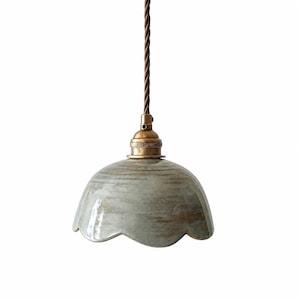 May include: A pendant light fixture featuring a scalloped, dome-shaped ceramic shade with a glossy, mottled gray and brown glaze. The shade is attached to a metallic brass-toned socket and hangs from a twisted brown fabric-covered electrical cord.