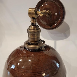 May include: A brown ceramic wall sconce with a brass socket and a brown ceramic shade. The sconce has a simple design and is perfect for adding a touch of rustic charm to any room.