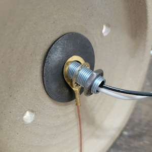 May include: Close-up of a brass electrical connector with a black and white wire attached to it. The connector is mounted on a ceramic surface.