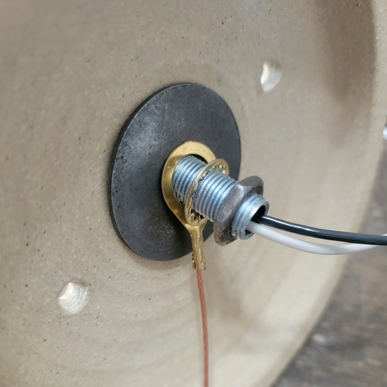May include: Close-up of a brass electrical connector with a black and white wire attached to it. The connector is mounted on a ceramic surface.