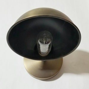 Peut inclure: Une applique murale en laiton avec un abat-jour noir et une ampoule transparente. L'applique a un design simple et moderne.