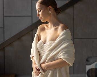 May include: A woman wearing a white beaded strapless dress with a white faux fur shawl draped over her shoulders.