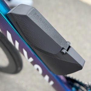 Puede incluir: Primer plano de una caja de almacenamiento gris montada en el cuadro de una bicicleta. La caja est&aacute; sujeta a una bicicleta con una combinaci&oacute;n de colores azul, morado y blanco. El texto "FOR K" es visible en la caja.