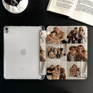 Puede incluir: Funda transparente para iPad con un collage de fotos familiares en la cubierta. El collage presenta m&uacute;ltiples retratos familiares en varias poses. El iPad est&aacute; sobre una superficie negra junto a un libro abierto y un objeto decorativo blanco.