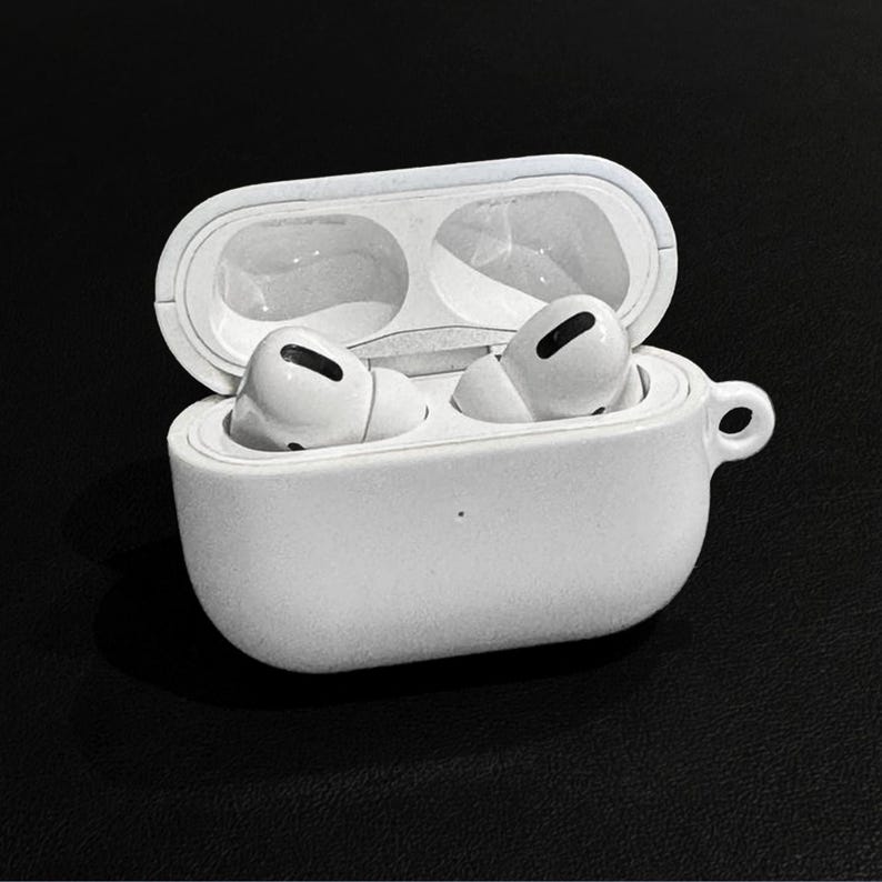 May include: White wireless earbuds in an open white charging case. The case has a small loop on the side. The earbuds are visible inside the case, ready for use. The background is black.