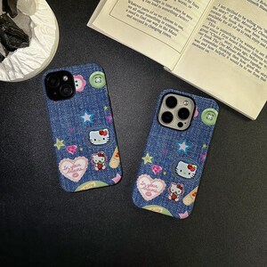 May include: Two blue denim iPhone cases featuring Hello Kitty and star designs. The cases include a pink heart with the text "In your dreams" and a white Hello Kitty character with a red bow.